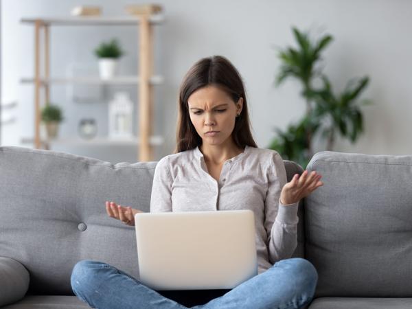 A frustrated woman on a sofa looking at her laptop
