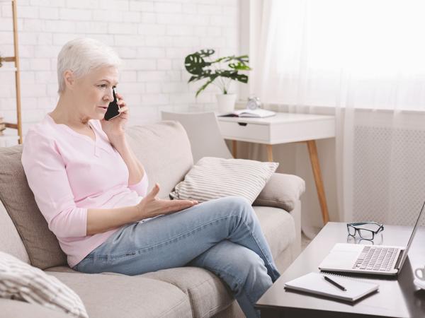 A woman on her sofa talking on the phone with a laptop open beside her