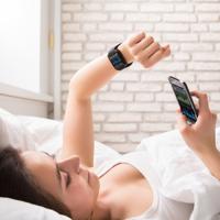 Woman synchronizing smartwatch with phone in bed